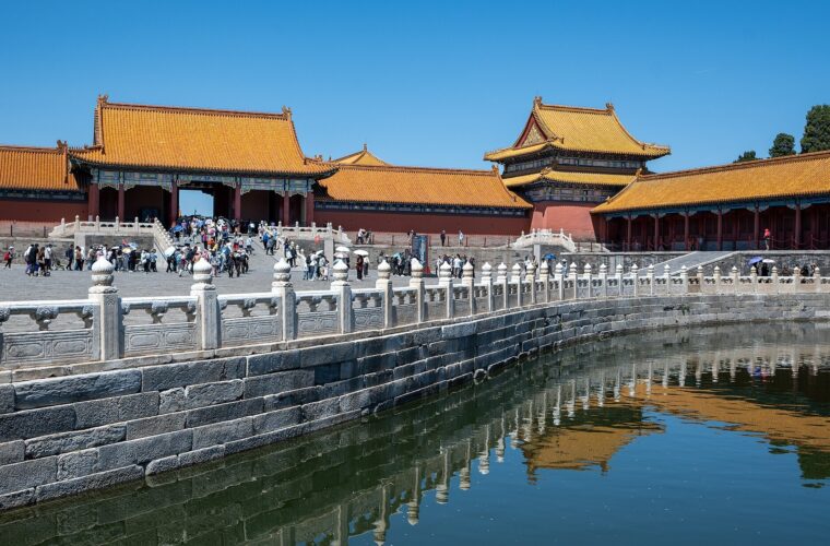 Visitors walk beside the Golden Water River in Beijing Forbidden City, where golden roofs and white balustrades reflect in the water.