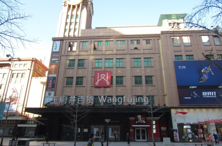 Wangfujing Department Store's clock tower and large bilingual lettering overlook pedestrians on the paved shopping street in Beijing.