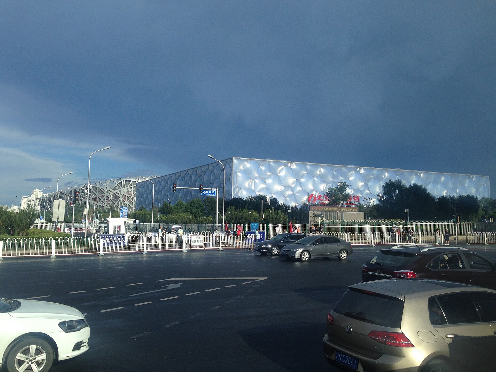 The Water Cube's bubble-patterned facade under a stormy sky, with the steel lattice of the Bird's Nest stadium visible to its left