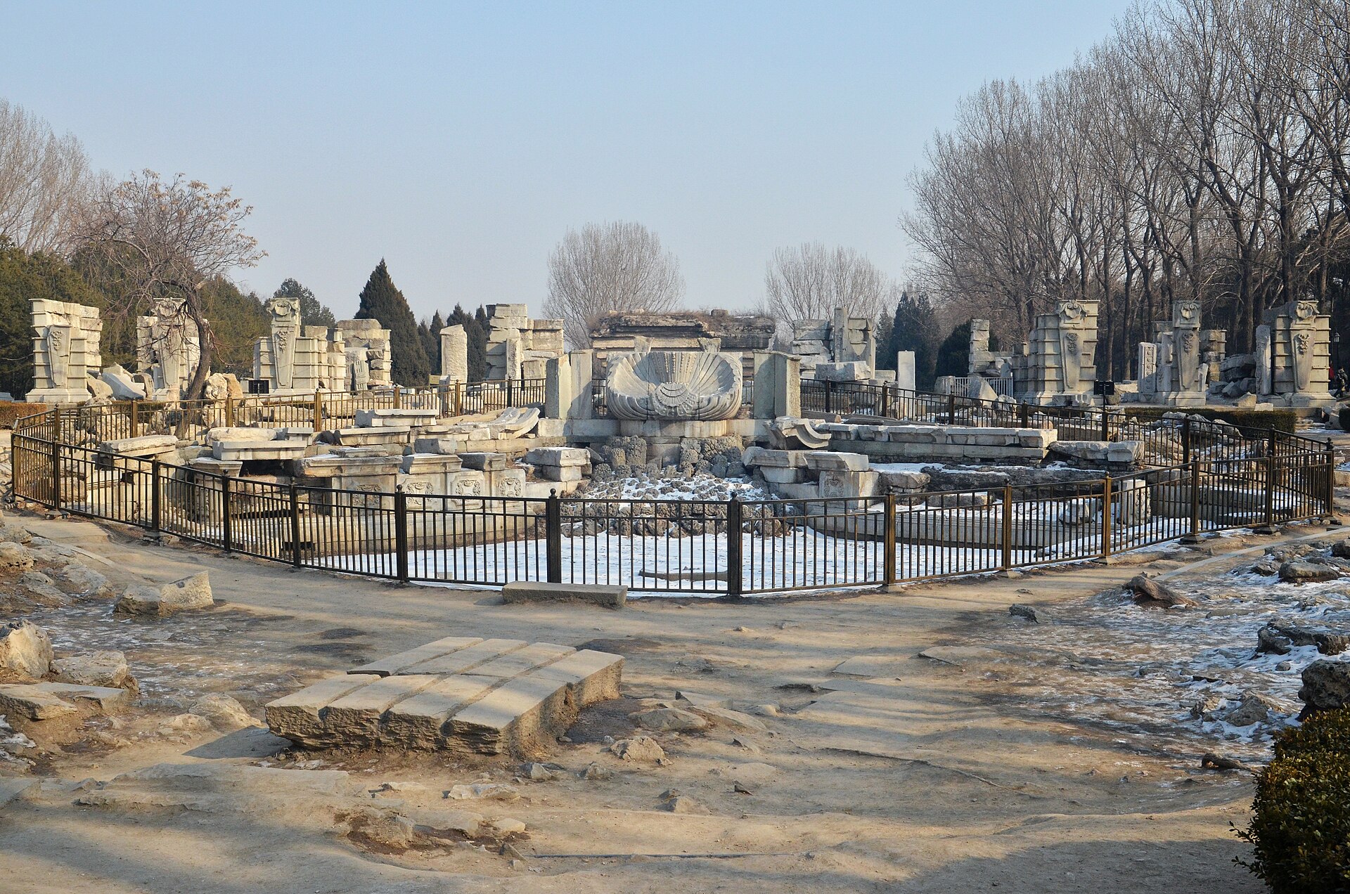 The fenced fountain basin of Haiyantang at Yuanmingyuan in winter, with a carved stone scallop shell at its centre and broken marble walls behind